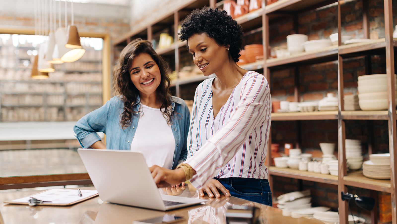 Duas empreendedoras sorridentes usando um notebook em sua loja